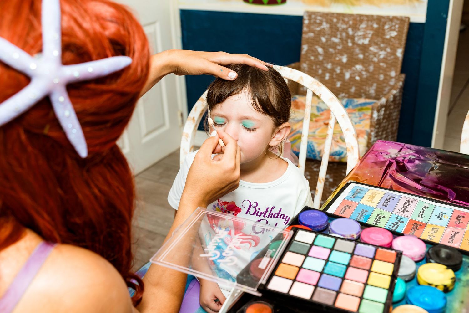 A child getting special party makeup applied from a colorful cosmetic palette at a themed celebration.