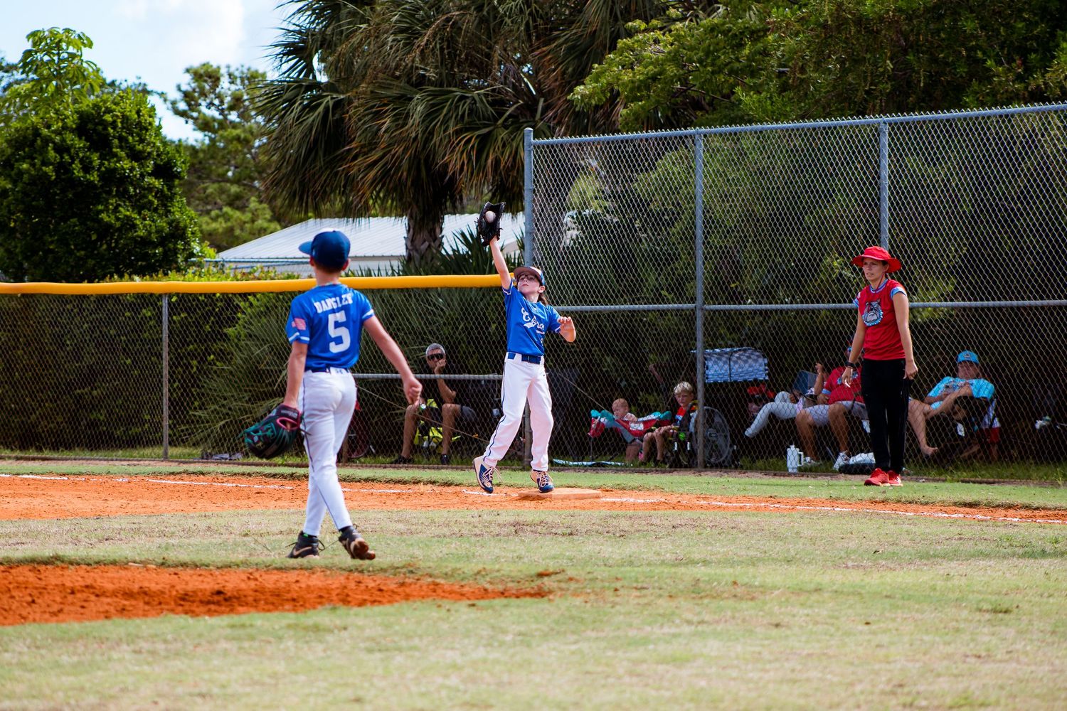 Youth baseball game in action with players in blue and red uniforms on a dirt diamond.