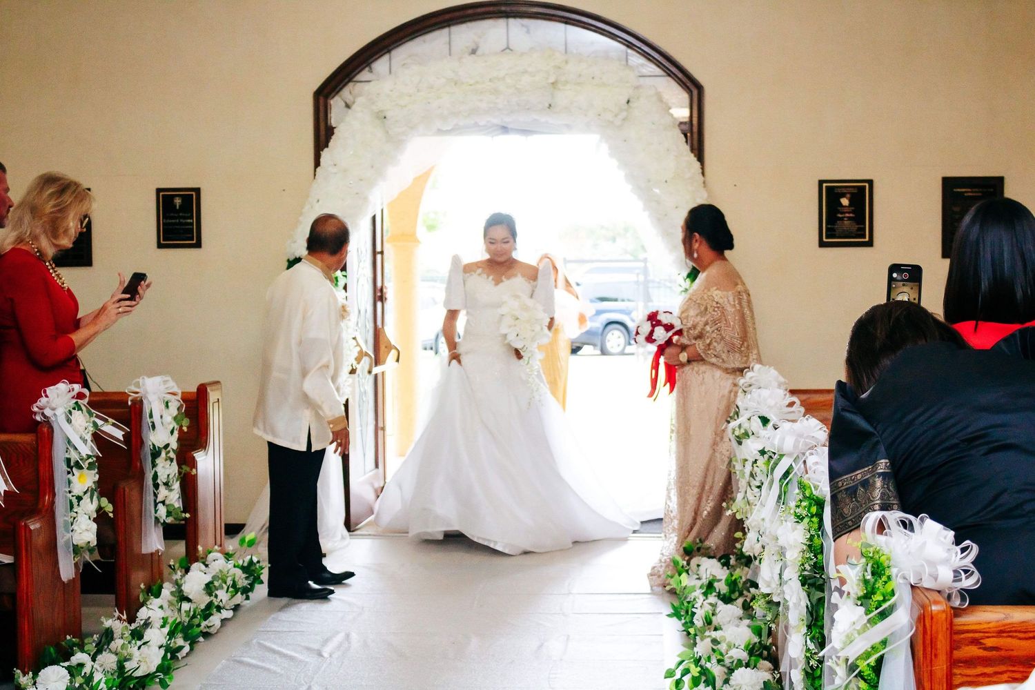 Interior of a chapel decorated with white floral arrangements along the aisle during a wedding ceremony.