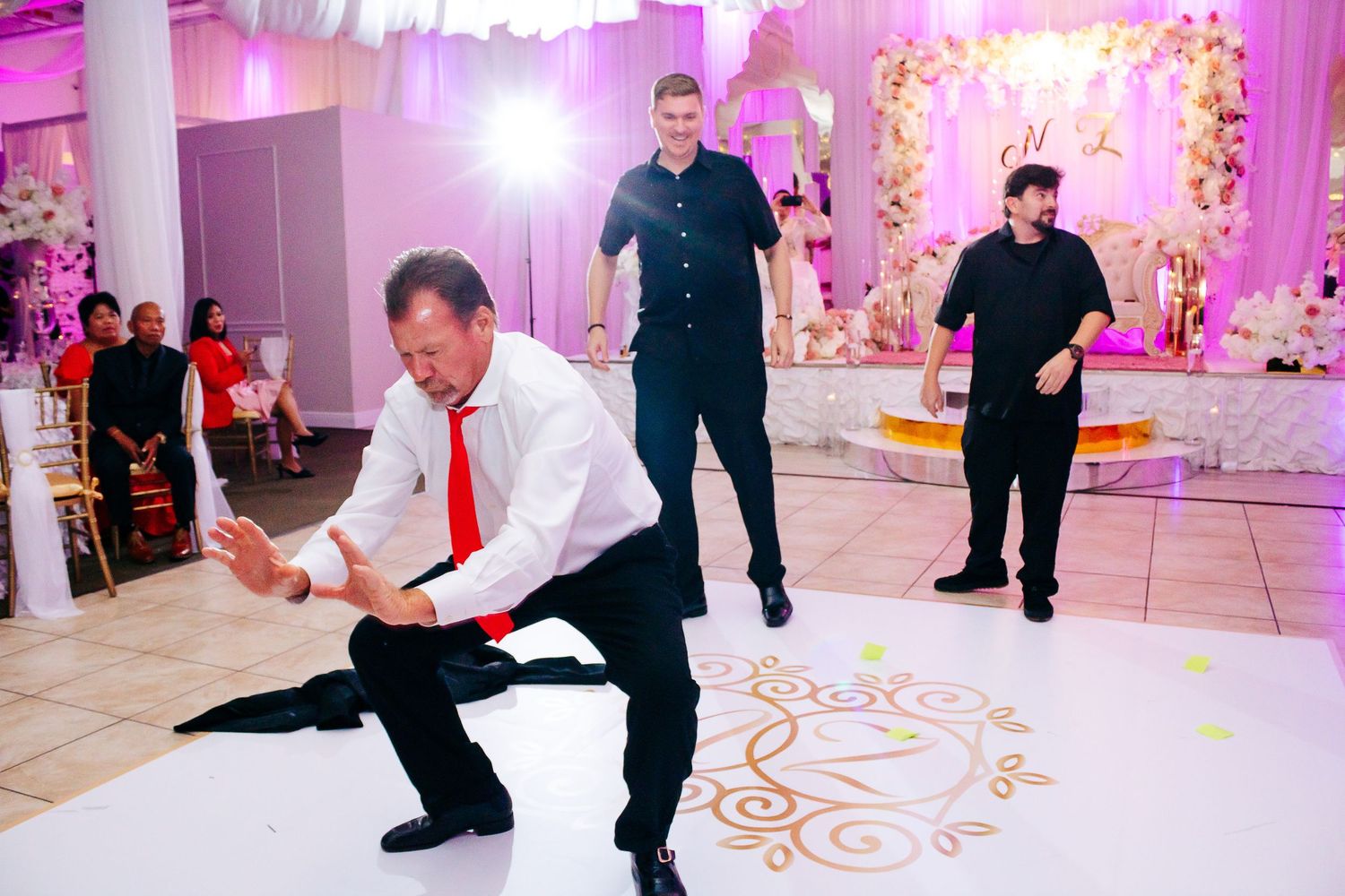 Wedding guests dancing on a beautifully decorated ballroom floor with pink ambient lighting.