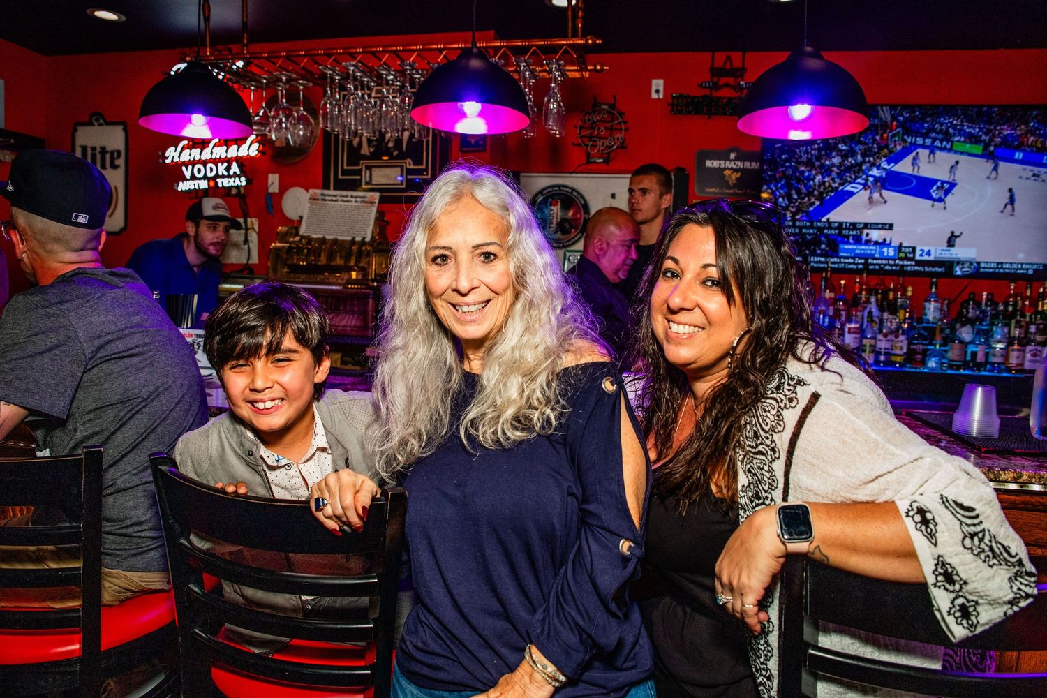 The image shows two women and a young boy posing together in what appears to be a bar or restaurant setting.