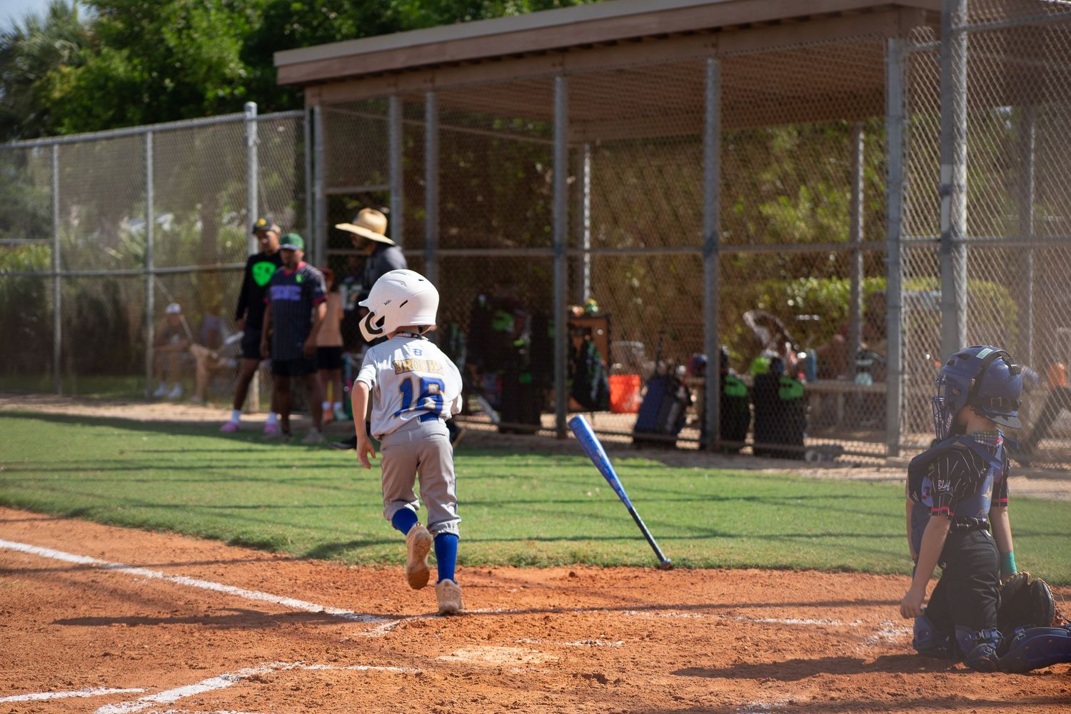 Baseball player at bat during a youth league game with dugout in background.