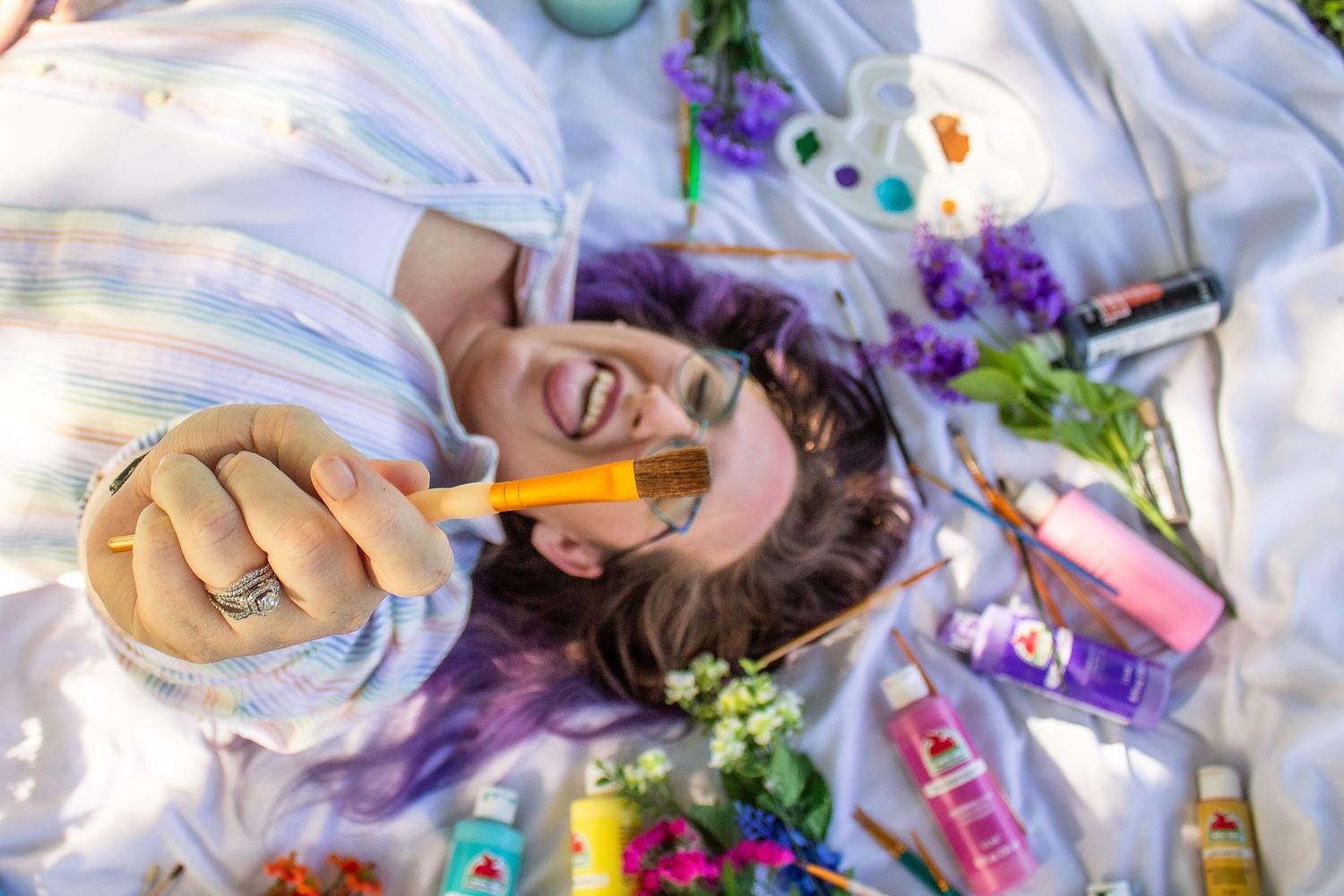 Overhead view of artist surrounded by colorful art supplies on white blanket.