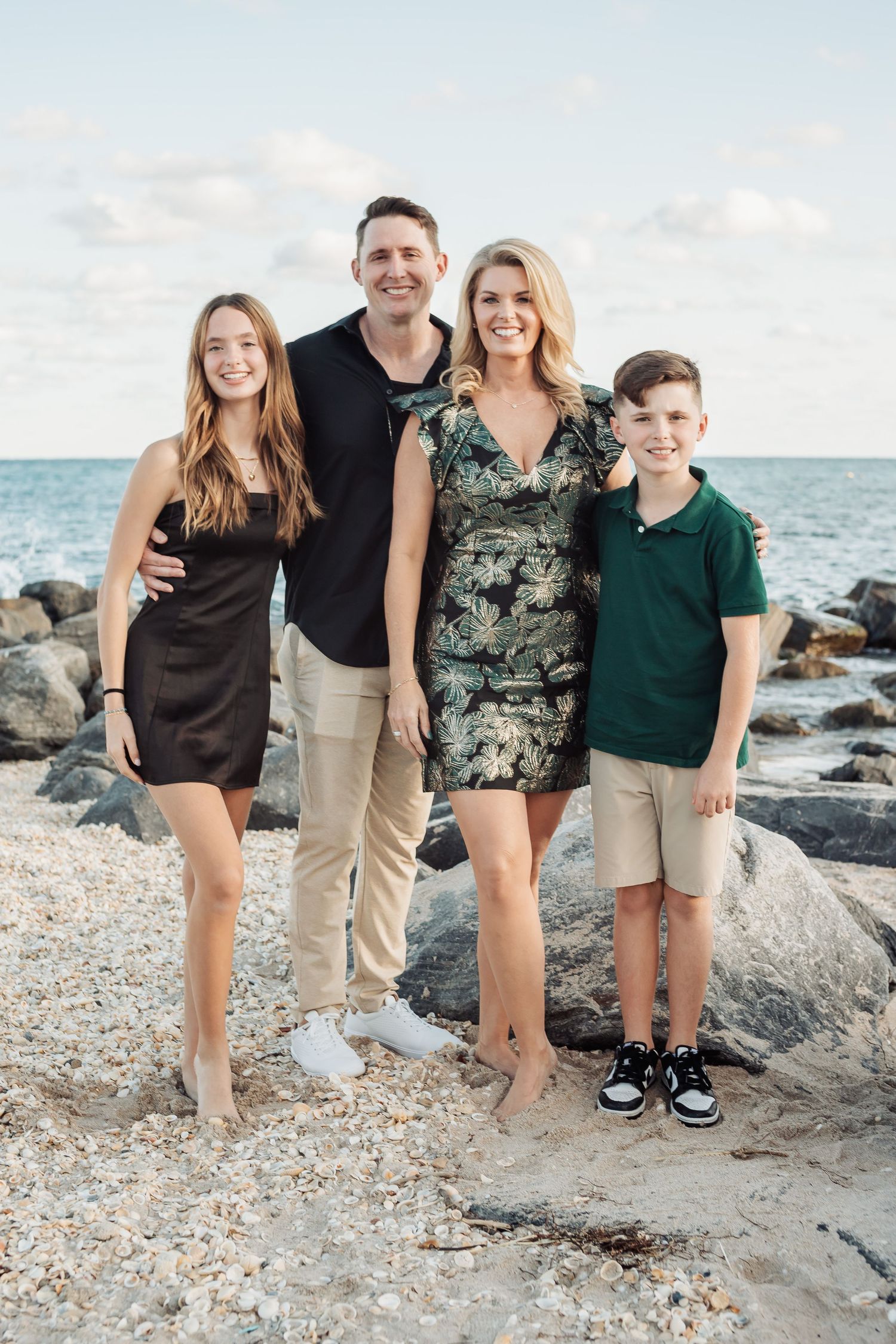 A family of four poses together on a rocky beach with the ocean and cloudy sky in the background.