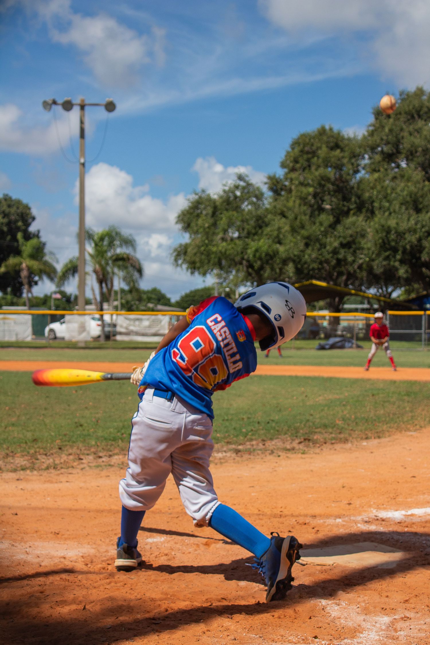 Baseball player in blue jersey swinging bat on dirt field during daytime game.