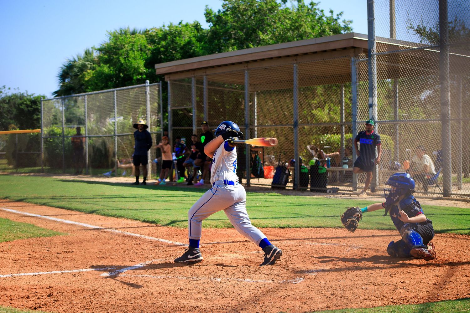 Baseball player swinging bat at home plate with catcher during sunny game.
