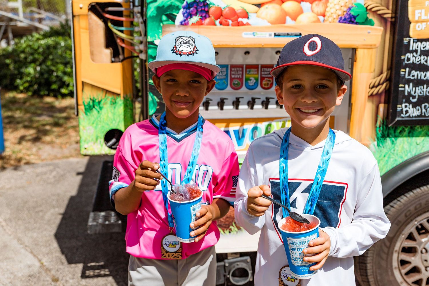 Two young friends enjoying colorful snow cones from a vending cart on a sunny day.