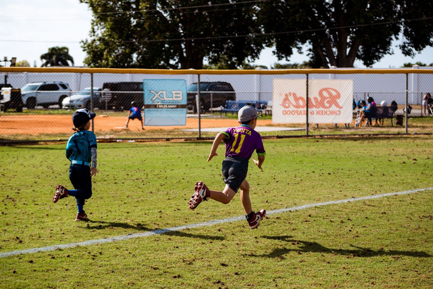 Children playing soccer on a grass field with buildings and graffiti in the background.