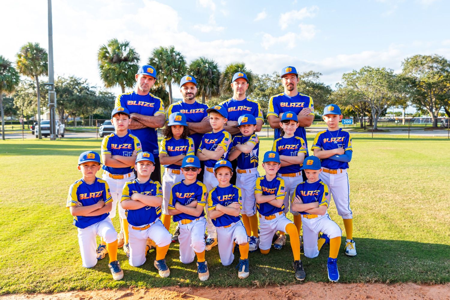 Youth baseball team in blue and white uniforms poses together on sunny field for team photo.