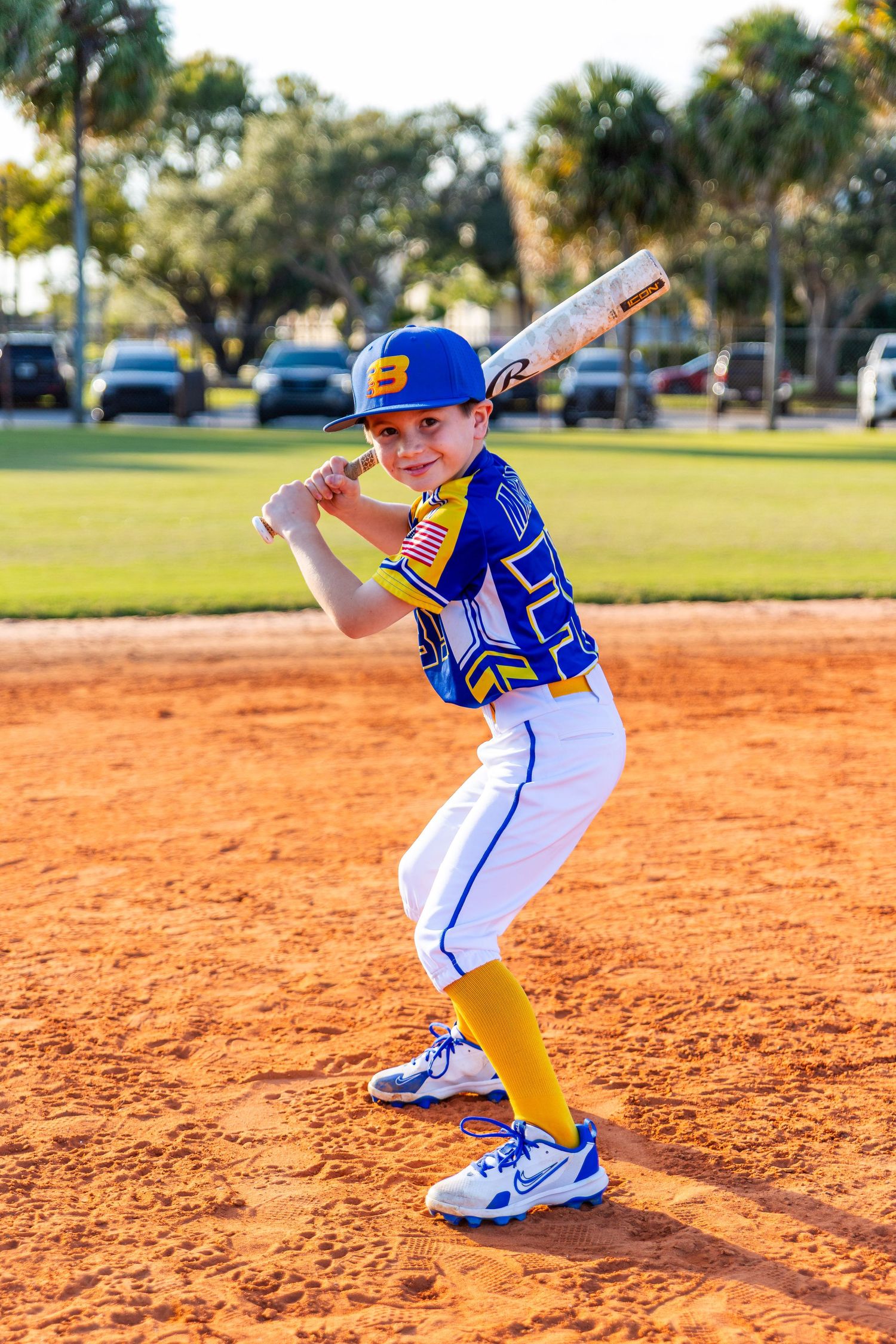 Young baseball player in blue and yellow uniform practicing batting stance on red clay baseball field.