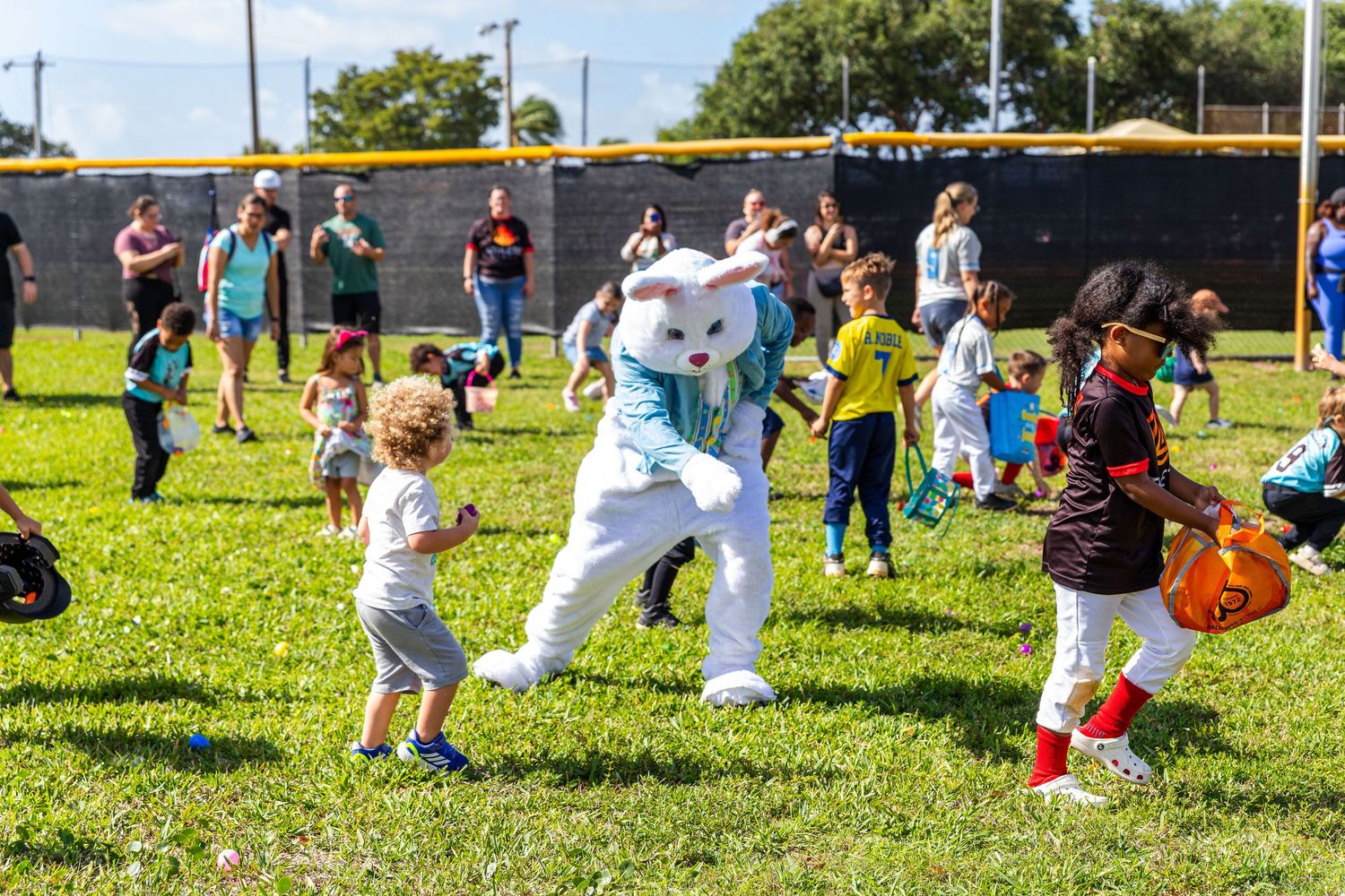 Children excitedly interact with the Easter Bunny mascot during an outdoor Easter egg hunt event.