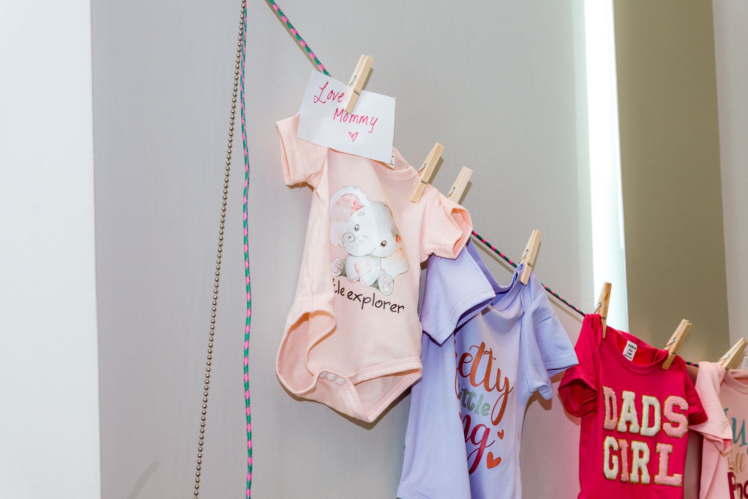 Baby clothes and onesies hanging on string display with clothespins at a shower party.