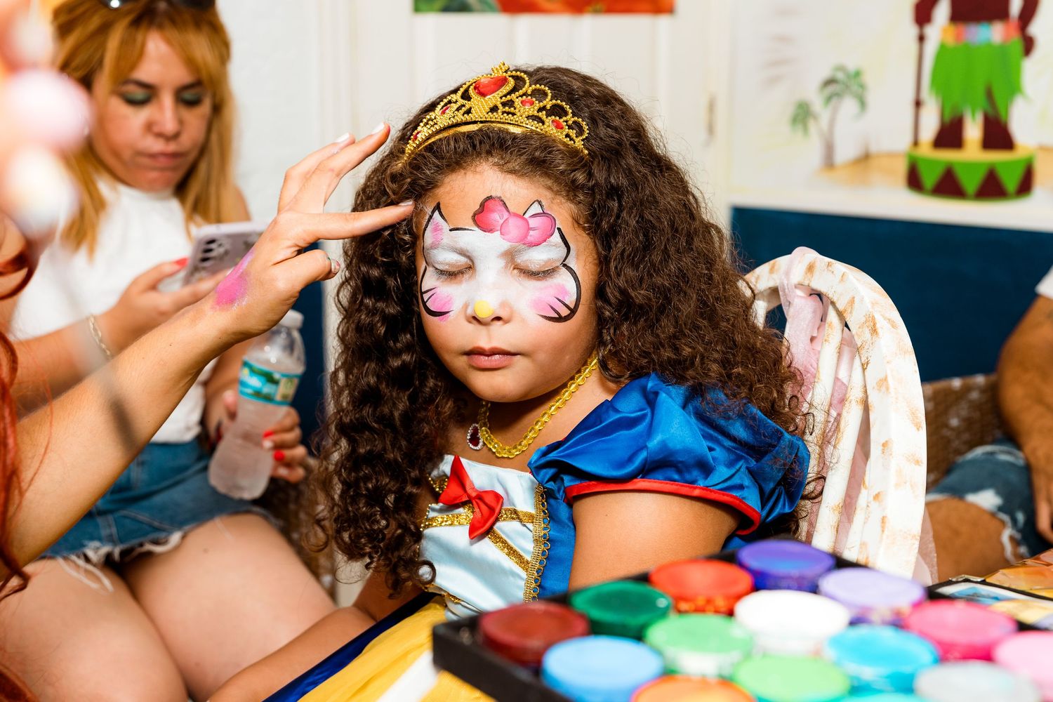 A young party guest getting detailed face painting with colorful designs and glitter.