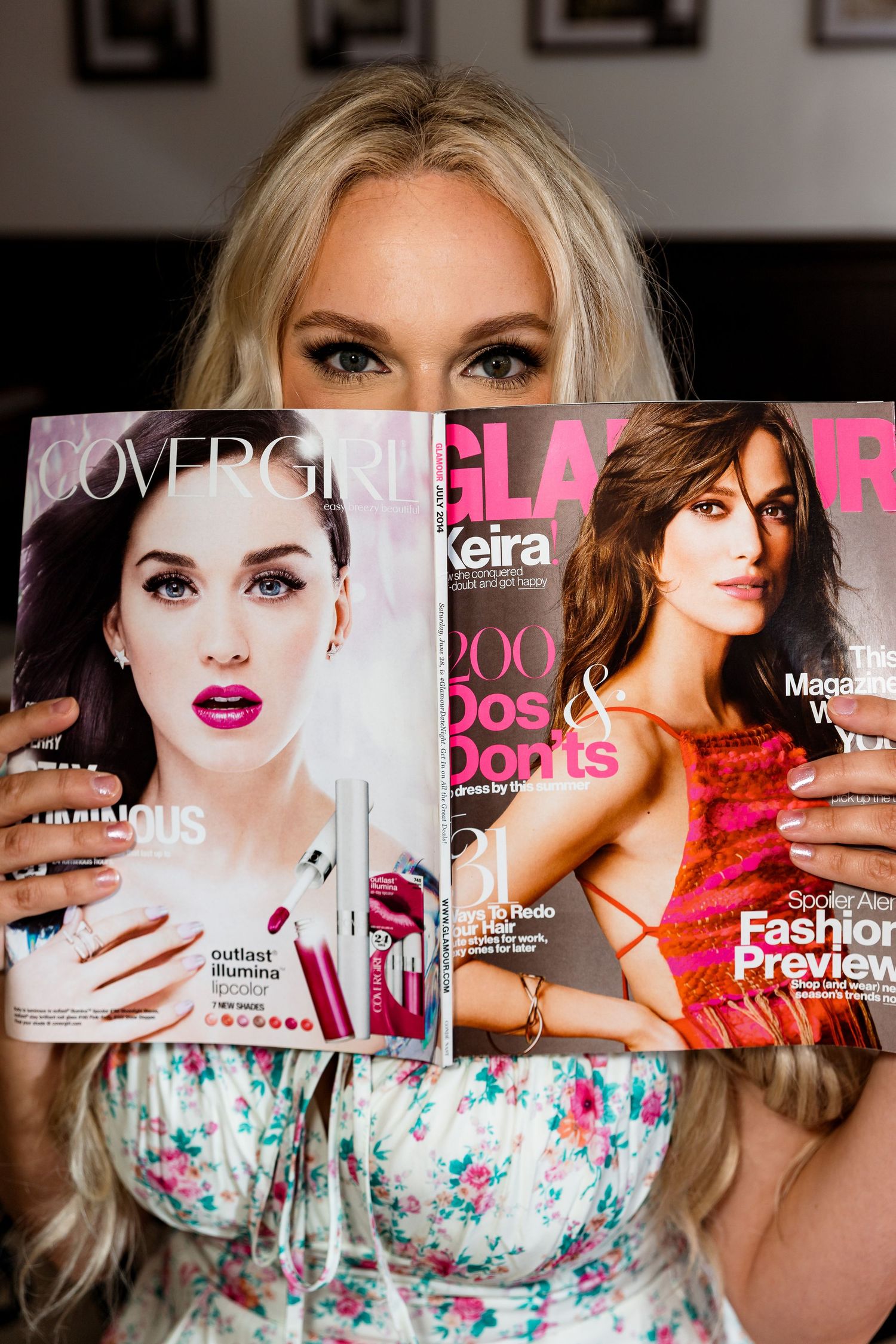 A woman holds up fashion magazines wearing a floral dress in a studio setting.