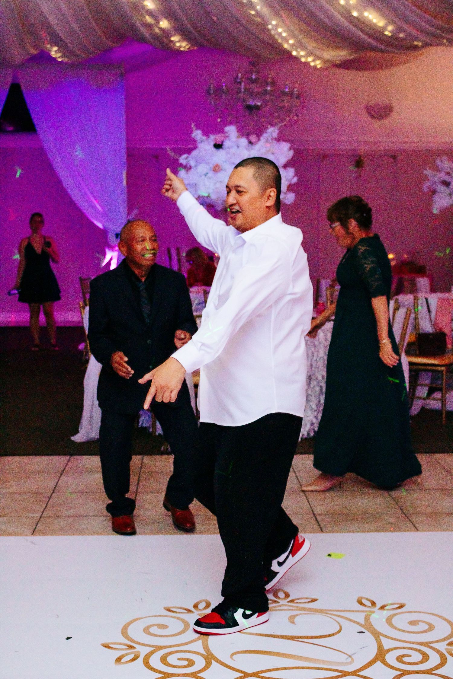 People dancing on a patterned dance floor at a reception with purple ambient lighting.