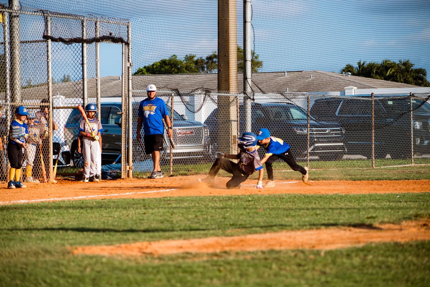 Youth baseball players compete in a game on a dirt and grass baseball diamond during a sunny afternoon.