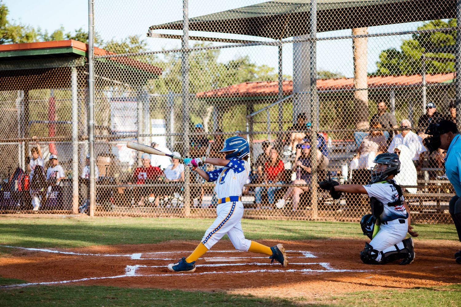 Baseball player in blue uniform swings bat at home plate during youth baseball game on sunny afternoon.