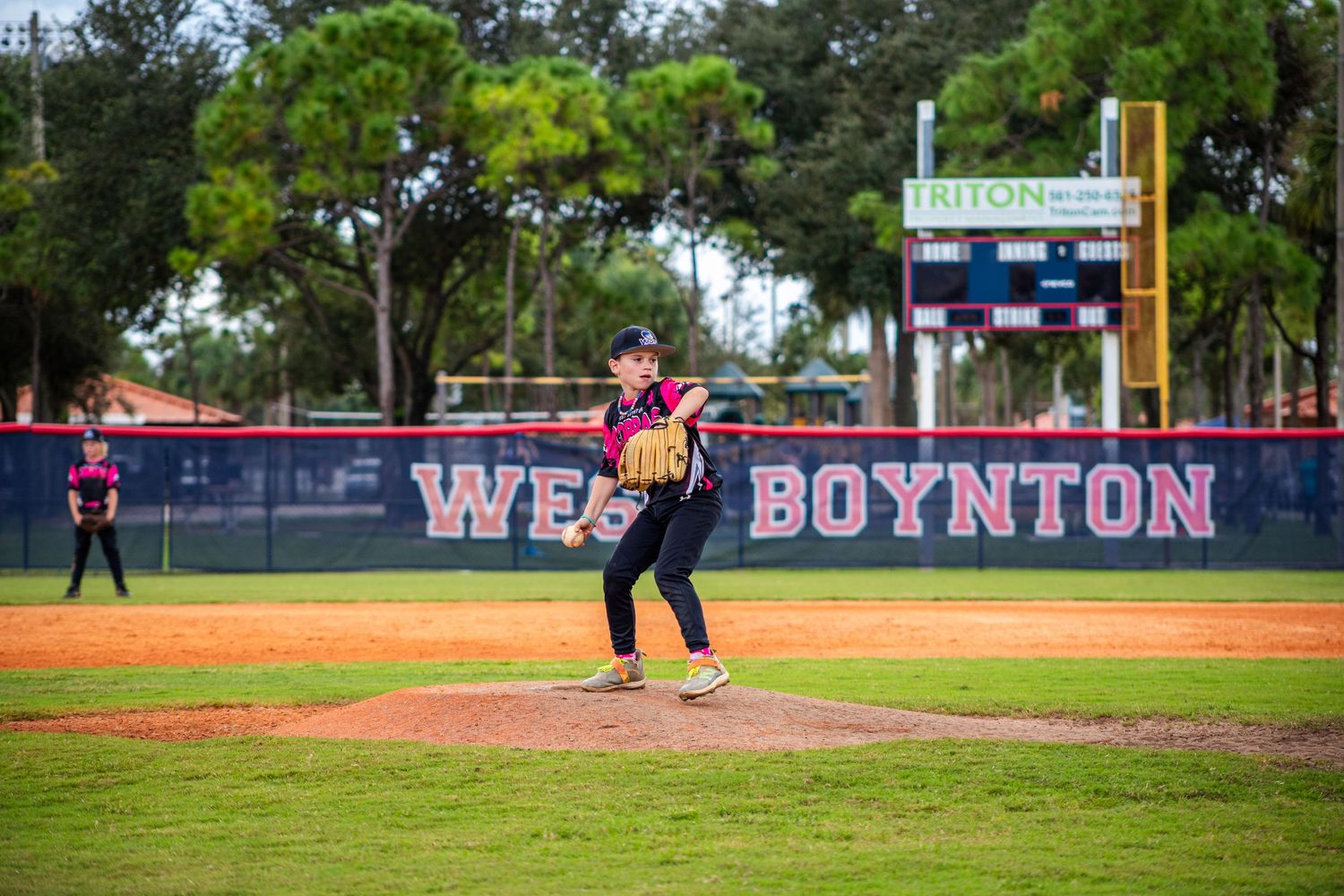 Baseball player in purple uniform stands ready on pitching mound at Boynton field during daytime game.