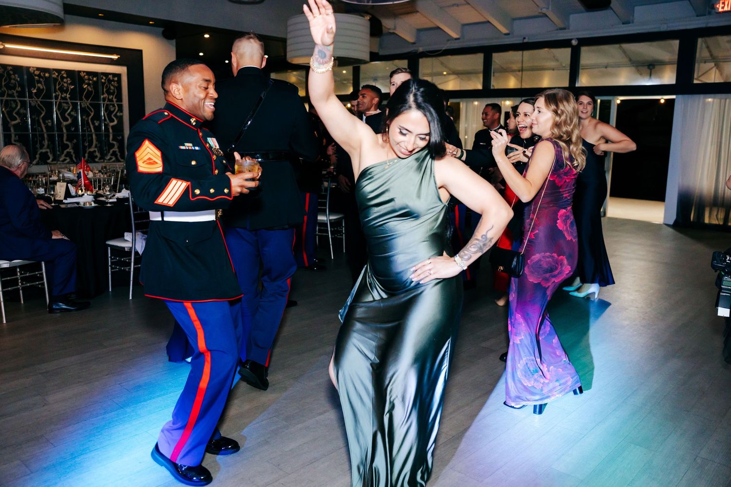 Guests dancing and mingling at formal military ball in dimly lit venue.