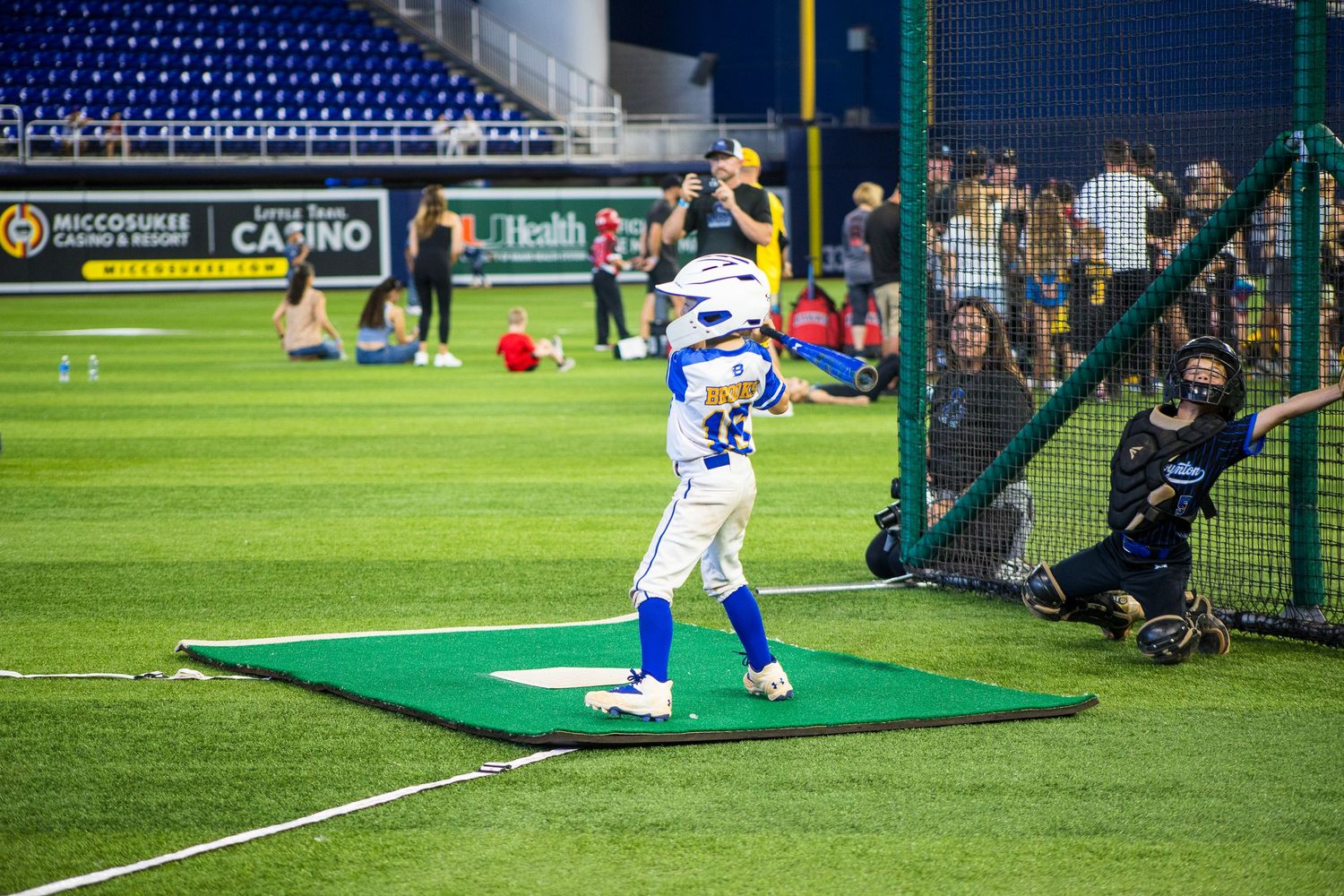 Baseball player takes practice swings in batting cage with catcher behind home plate.