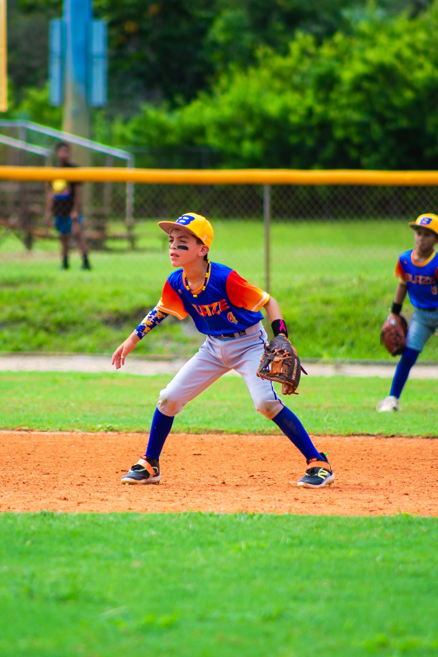 A baseball player in blue and orange uniform takes a defensive stance on the infield dirt.