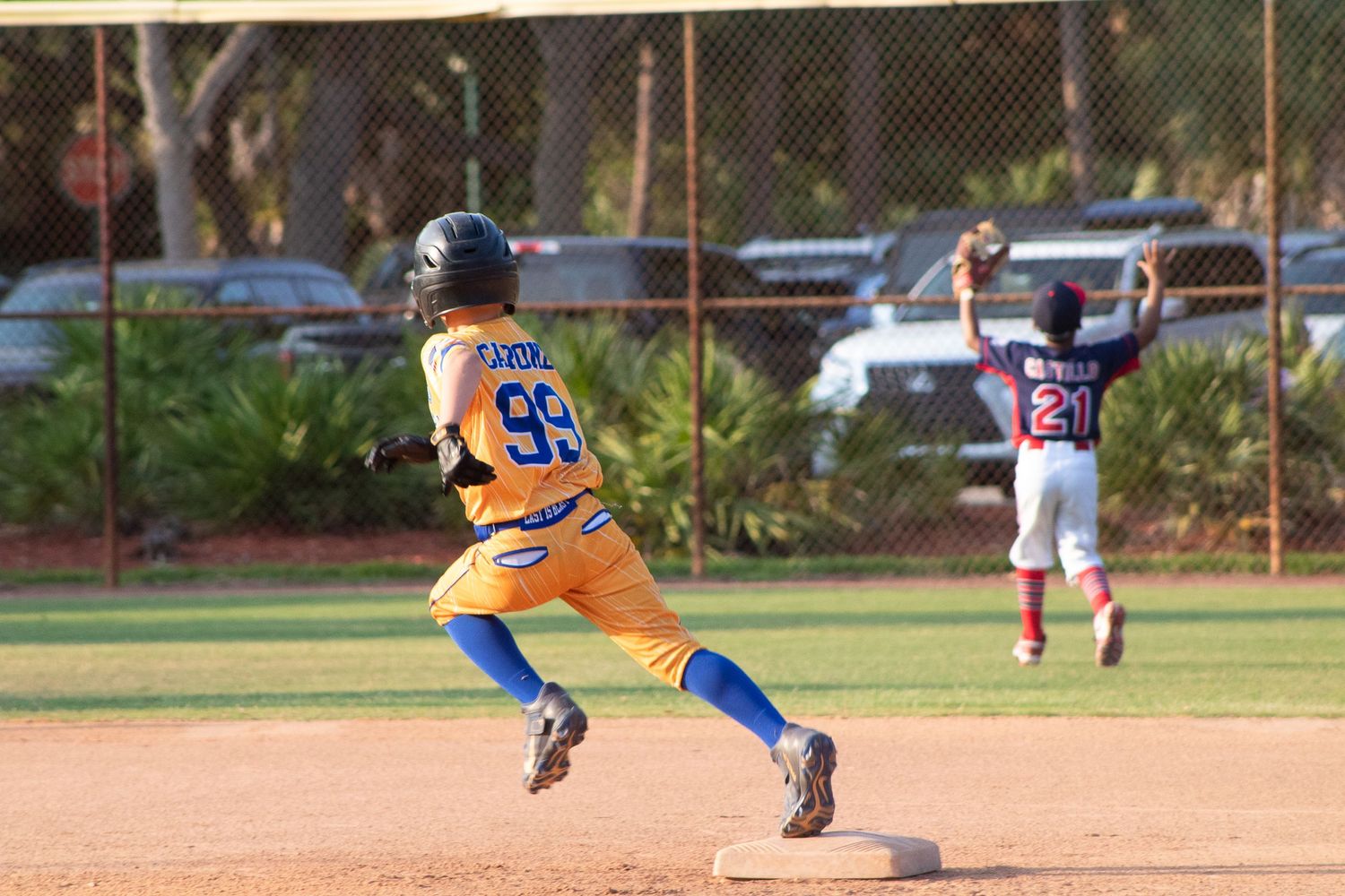 Baseball player in yellow uniform running between bases during youth league game.