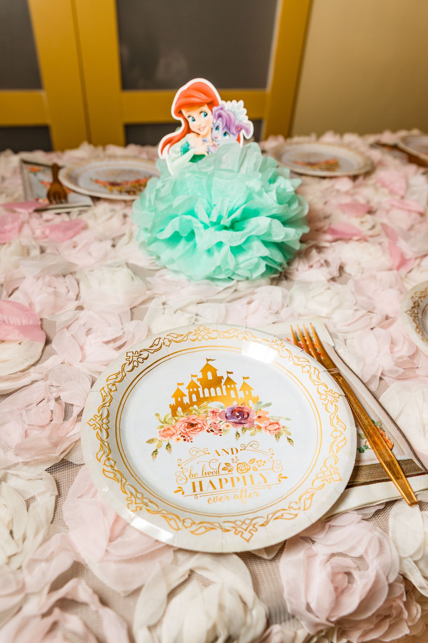 Little Mermaid themed party table setting with mint and pink decor, gold rimmed plates, and delicate flower petals.
