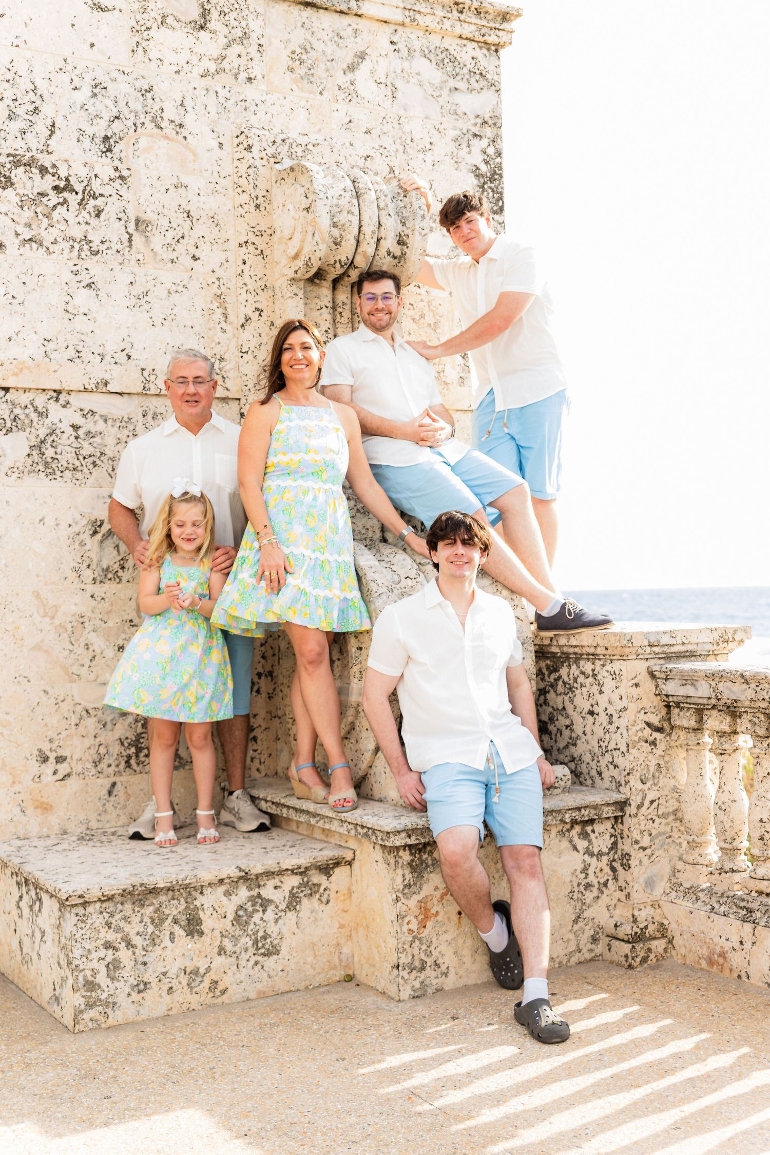 A group poses on weathered stone steps against a textured wall wearing coordinated summer outfits in white and mint green.