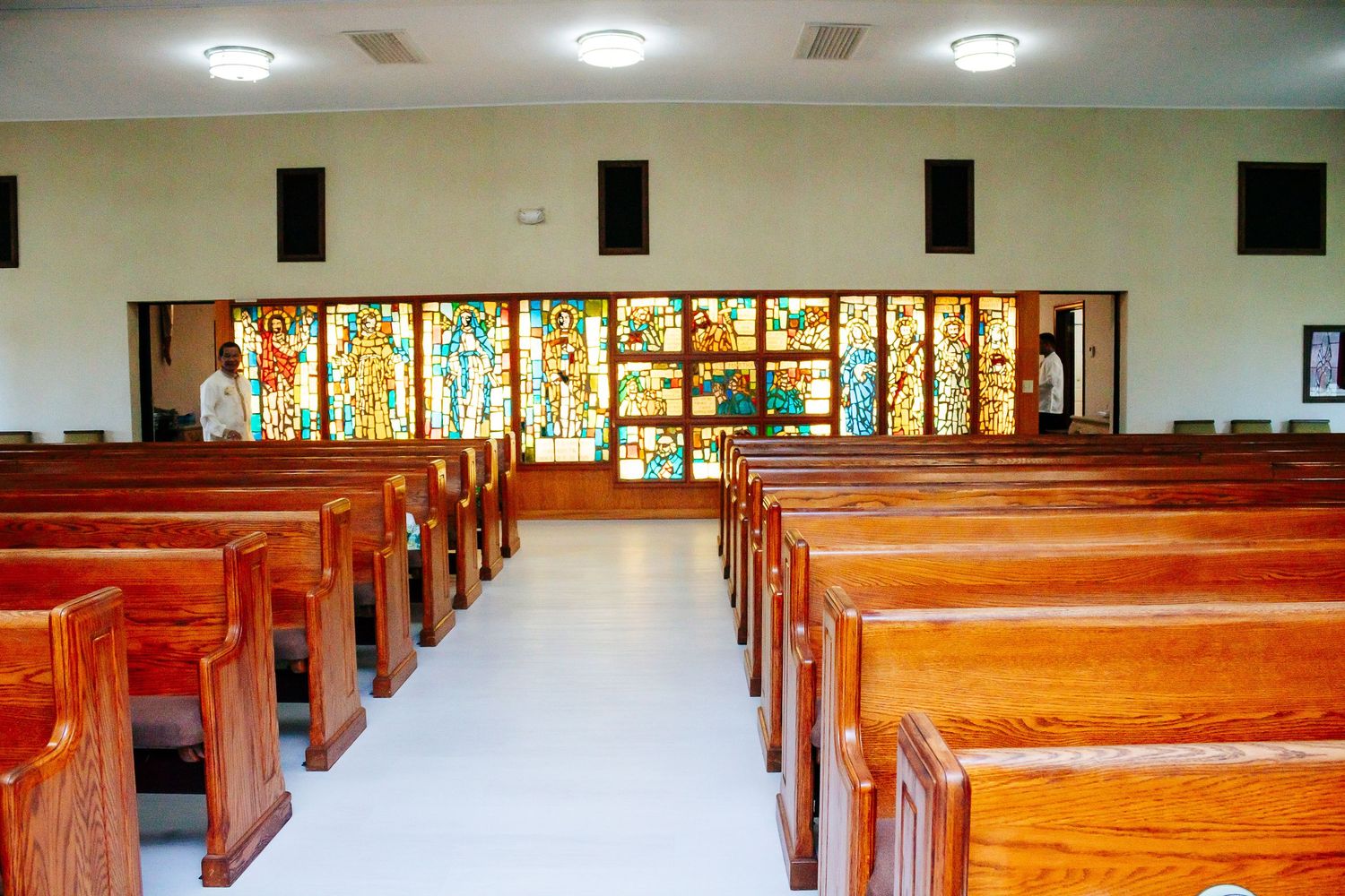Wooden church pews lined up in rows with stained glass windows visible in a traditional chapel interior.