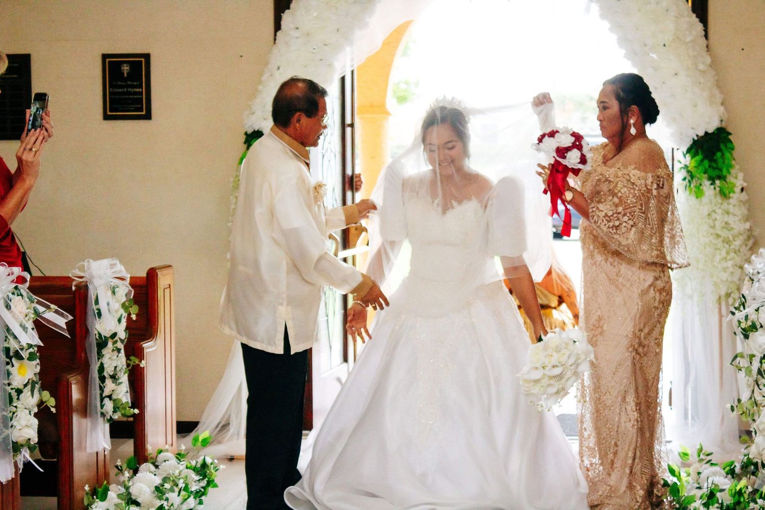 Beautiful wedding ceremony in a church with white floral decor and a flowing white bridal gown.