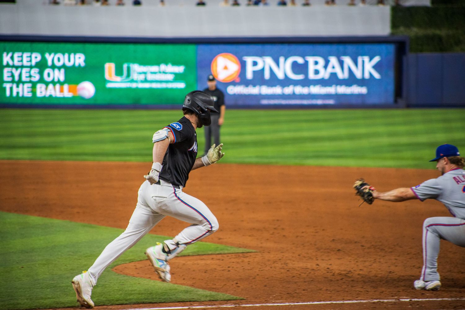 Baseball players in action on field with PNC Bank advertisement visible in background.