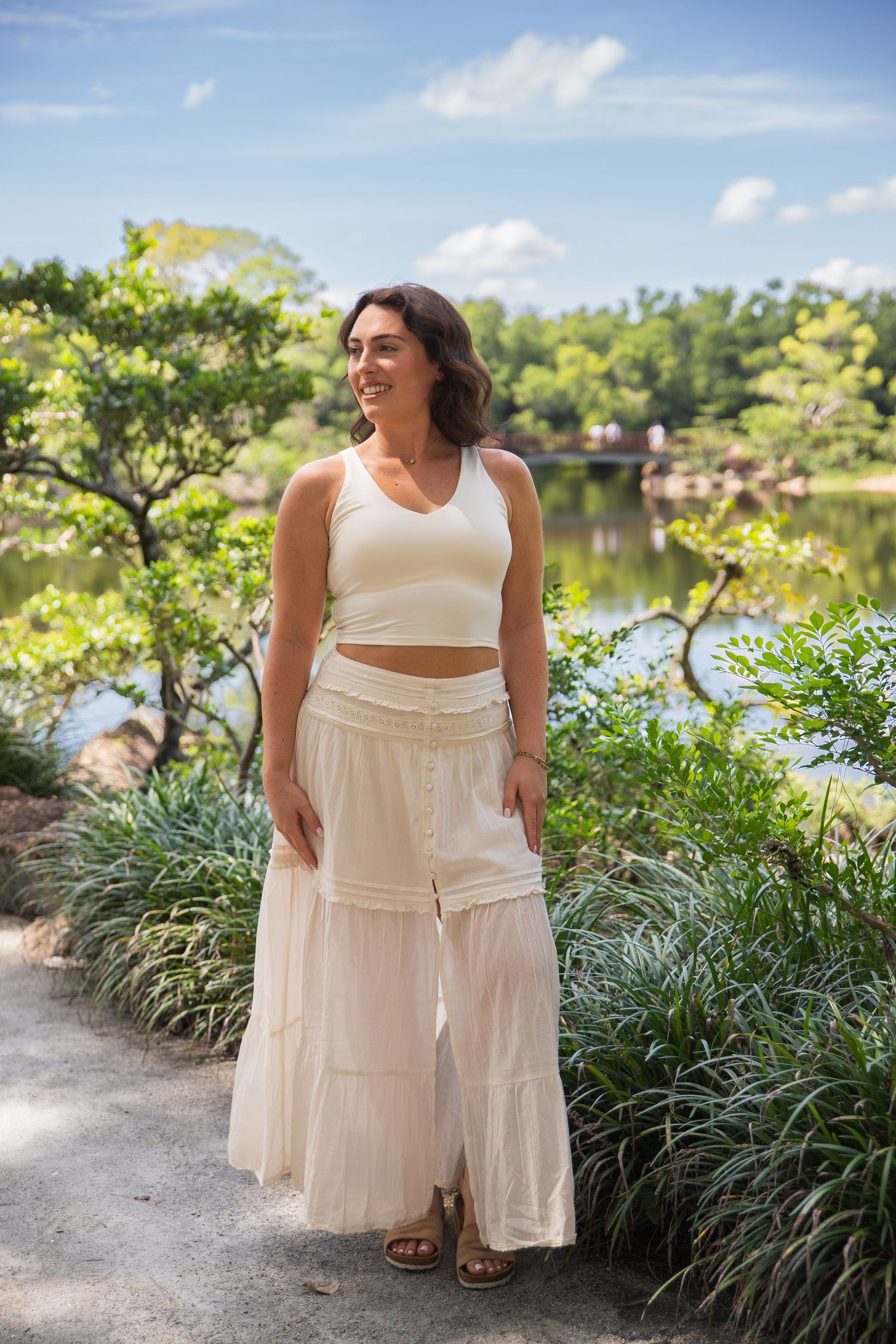 A summer fashion photoshoot in a garden path with a flowing cream-colored outfit and natural lighting.