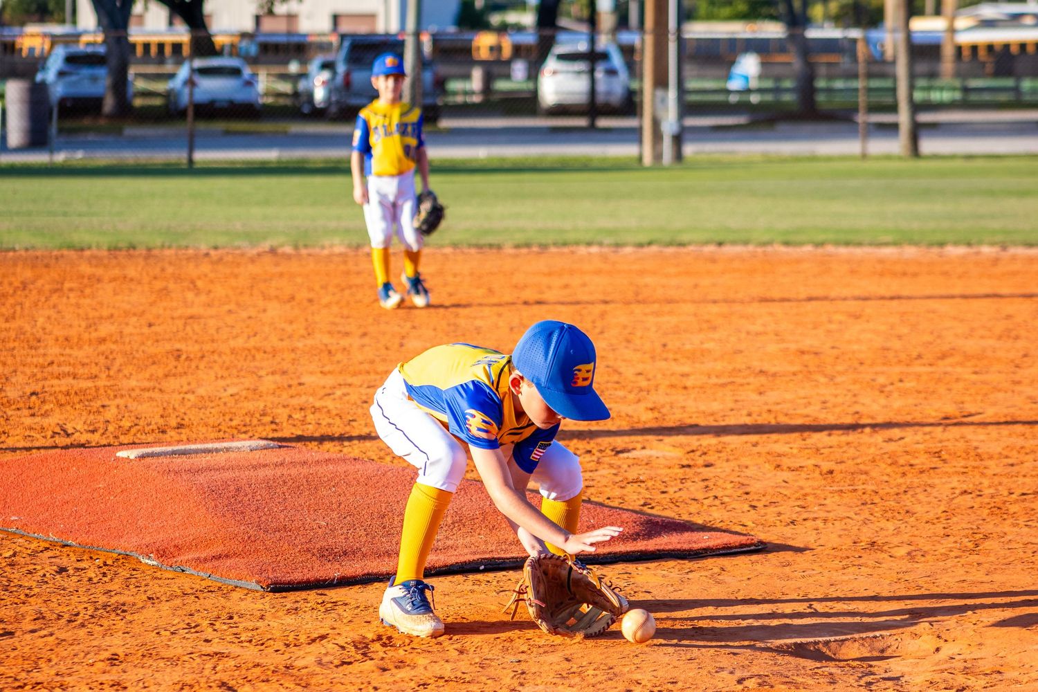 Baseball player sliding into base during game on dirt infield while opponent attempts to make the tag.
