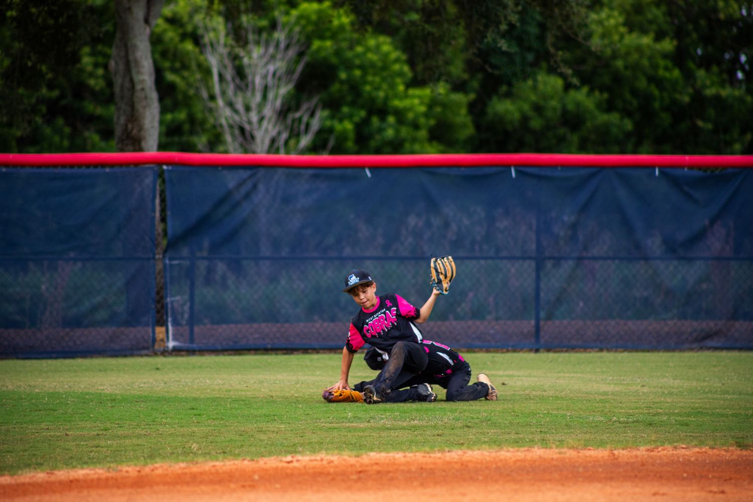 Baseball player makes diving catch attempt in outfield grass during game.