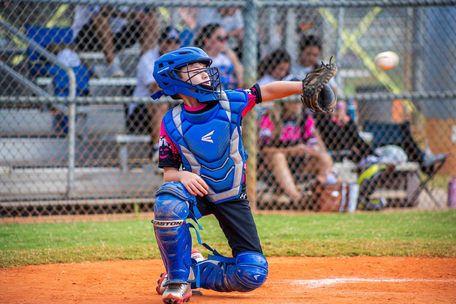 A baseball player in blue and orange uniform crouches behind home plate during a game.