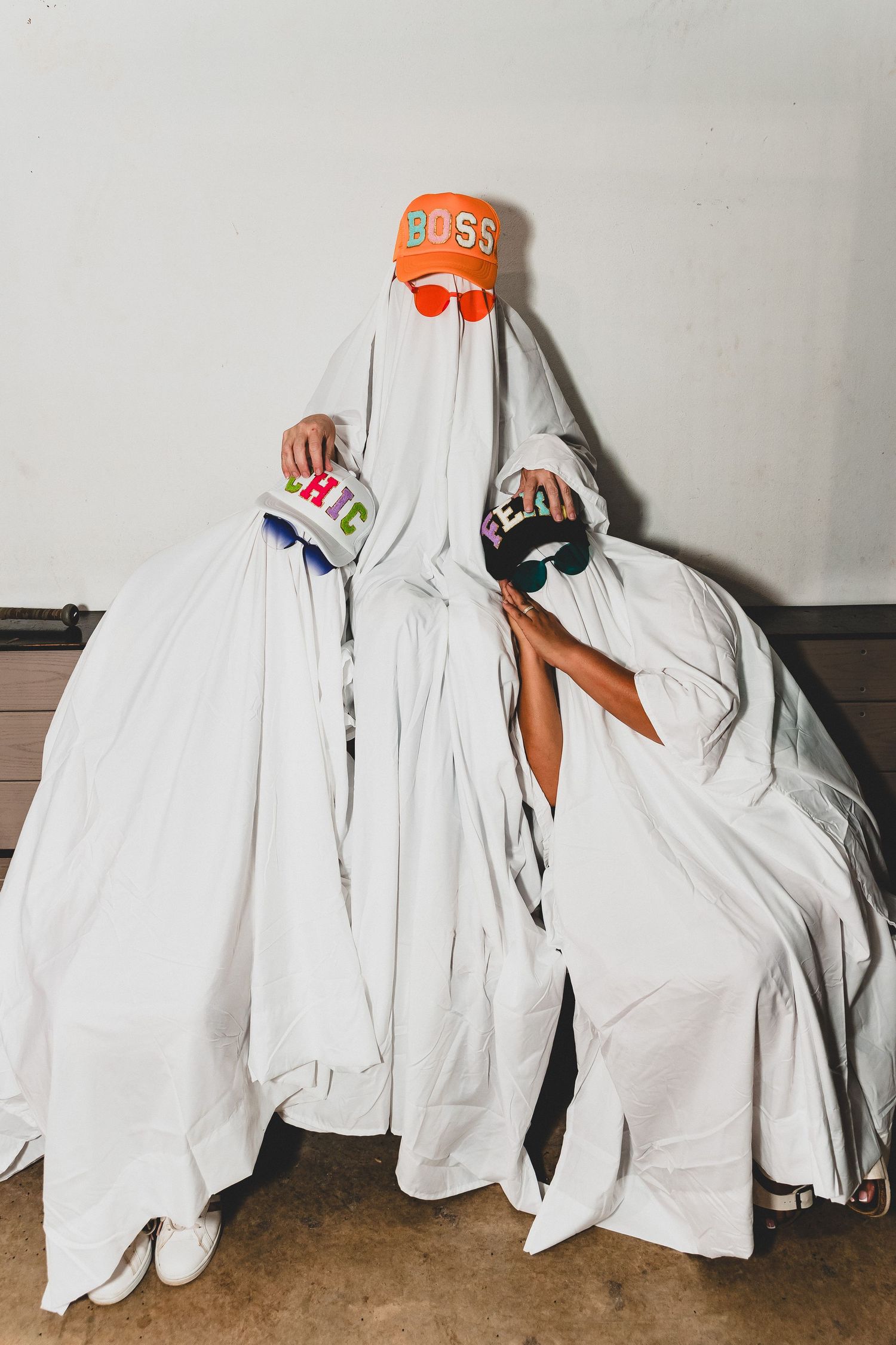 Row of white ghost costumes with orange accessories arranged against a light gray wall.