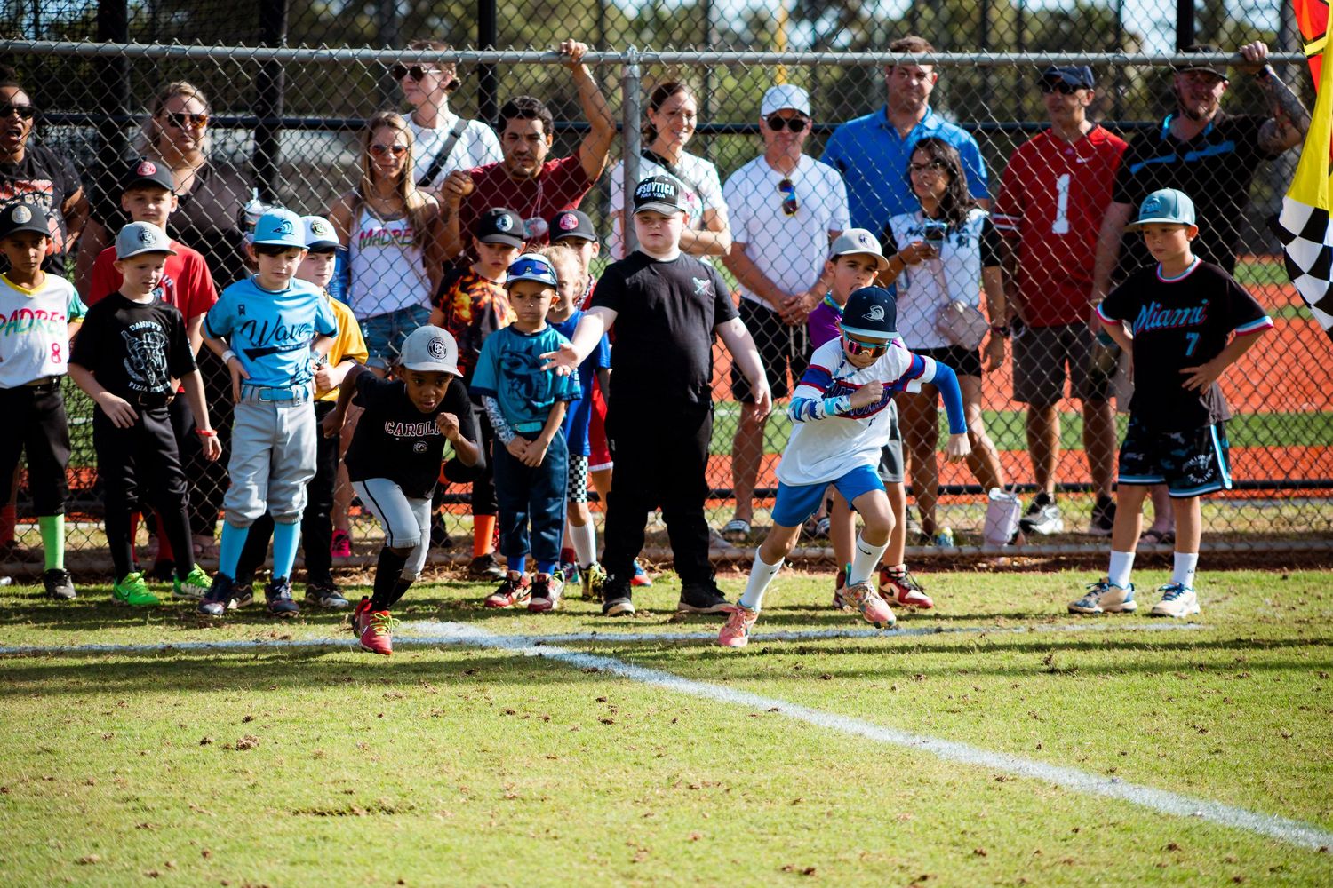 Youth baseball players and spectators gather on a sunny day at a baseball field during a sports activity.