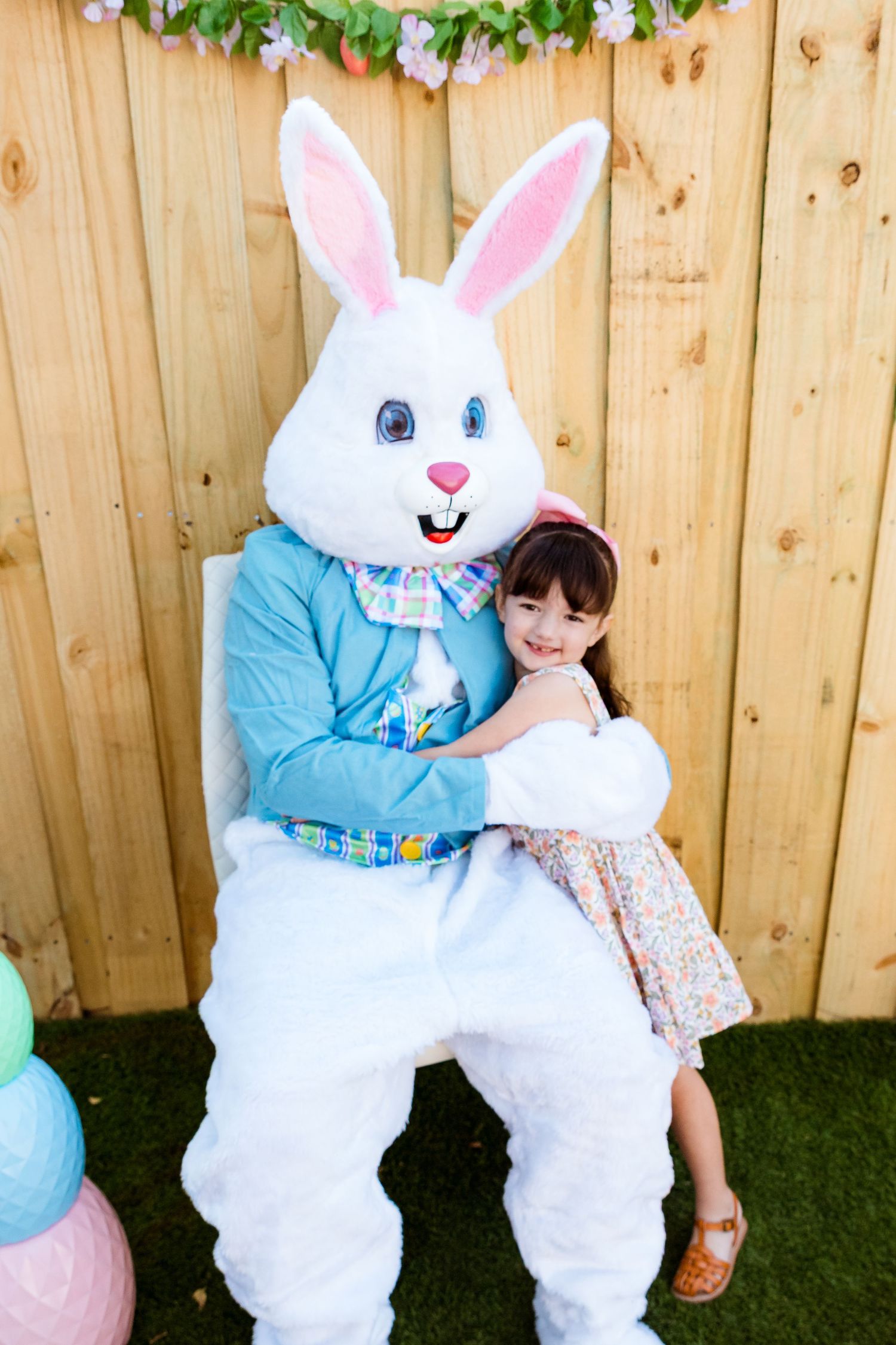 Easter bunny character in blue vest hugging visitor against wooden fence backdrop.