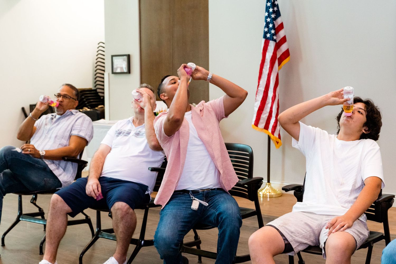 Group of people playfully pose with silly expressions in a room with an American flag.