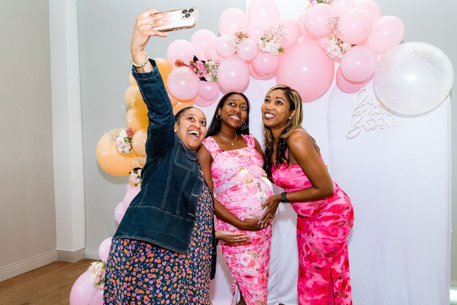 Friends taking selfies in front of pink balloon decorations at celebration.