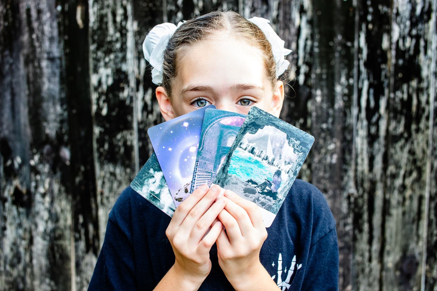 Young person holding up mystical tarot cards while wearing hairbows.