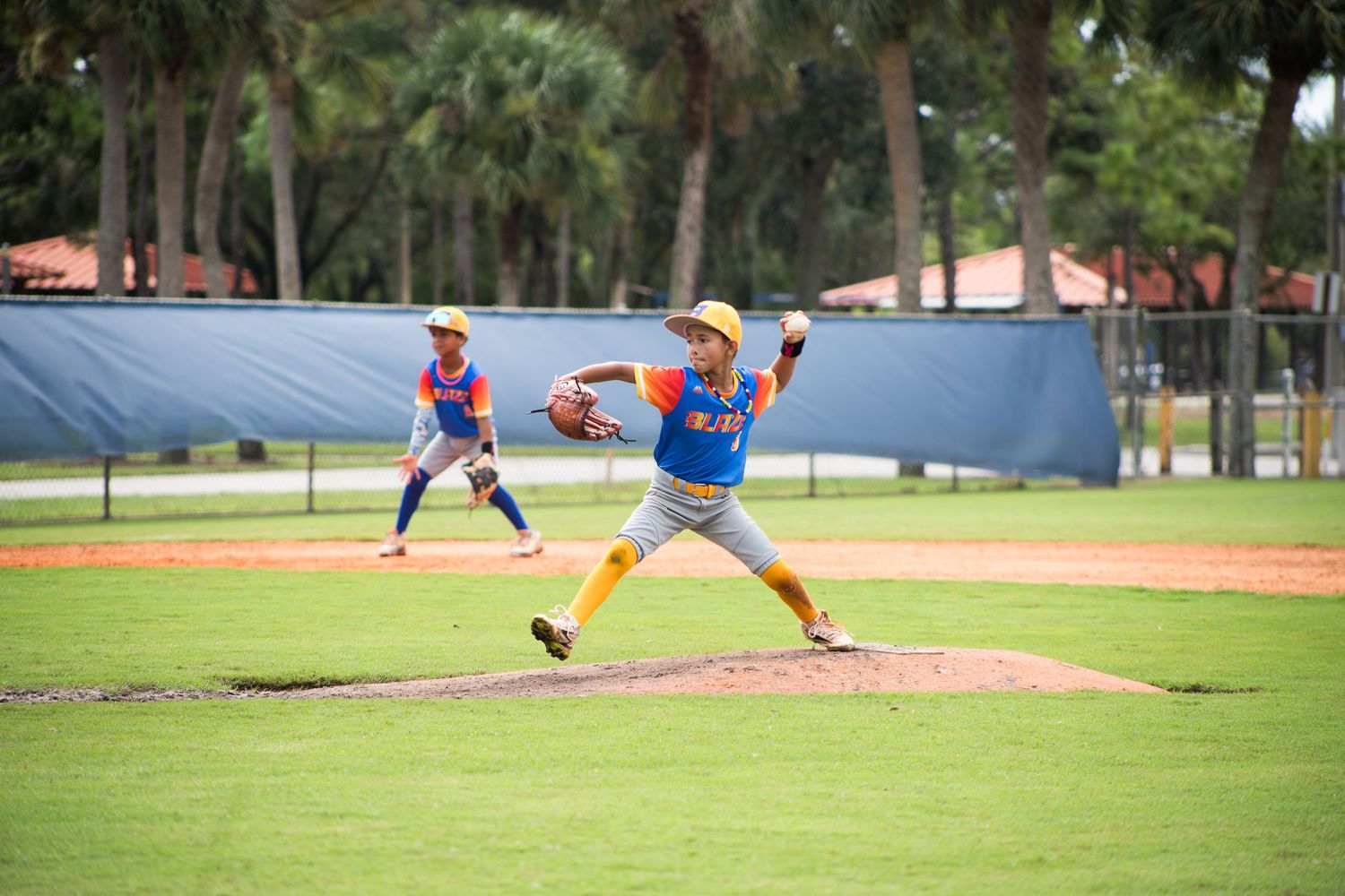 Pitcher in orange and blue uniform showing dynamic throwing motion on baseball field.