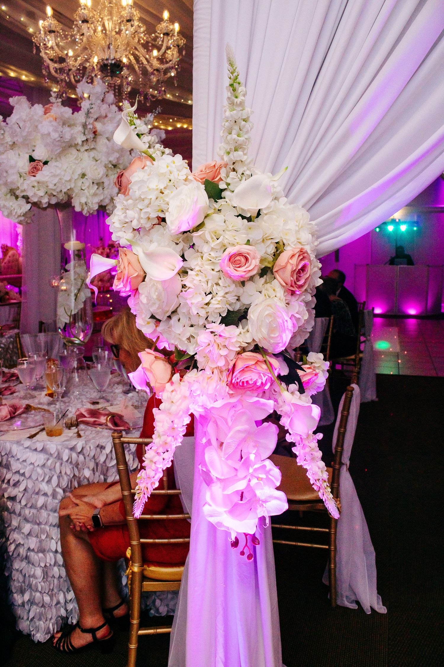Ornate floral arrangement with pink and white flowers illuminated by purple uplighting.