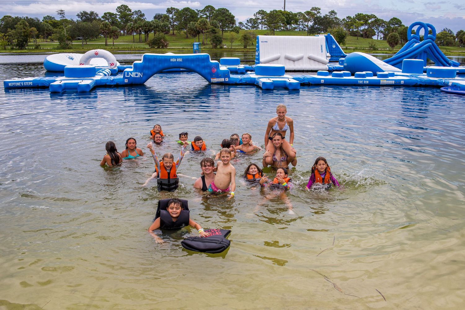People having fun in a shallow water park area with inflatable obstacle courses and water features.
