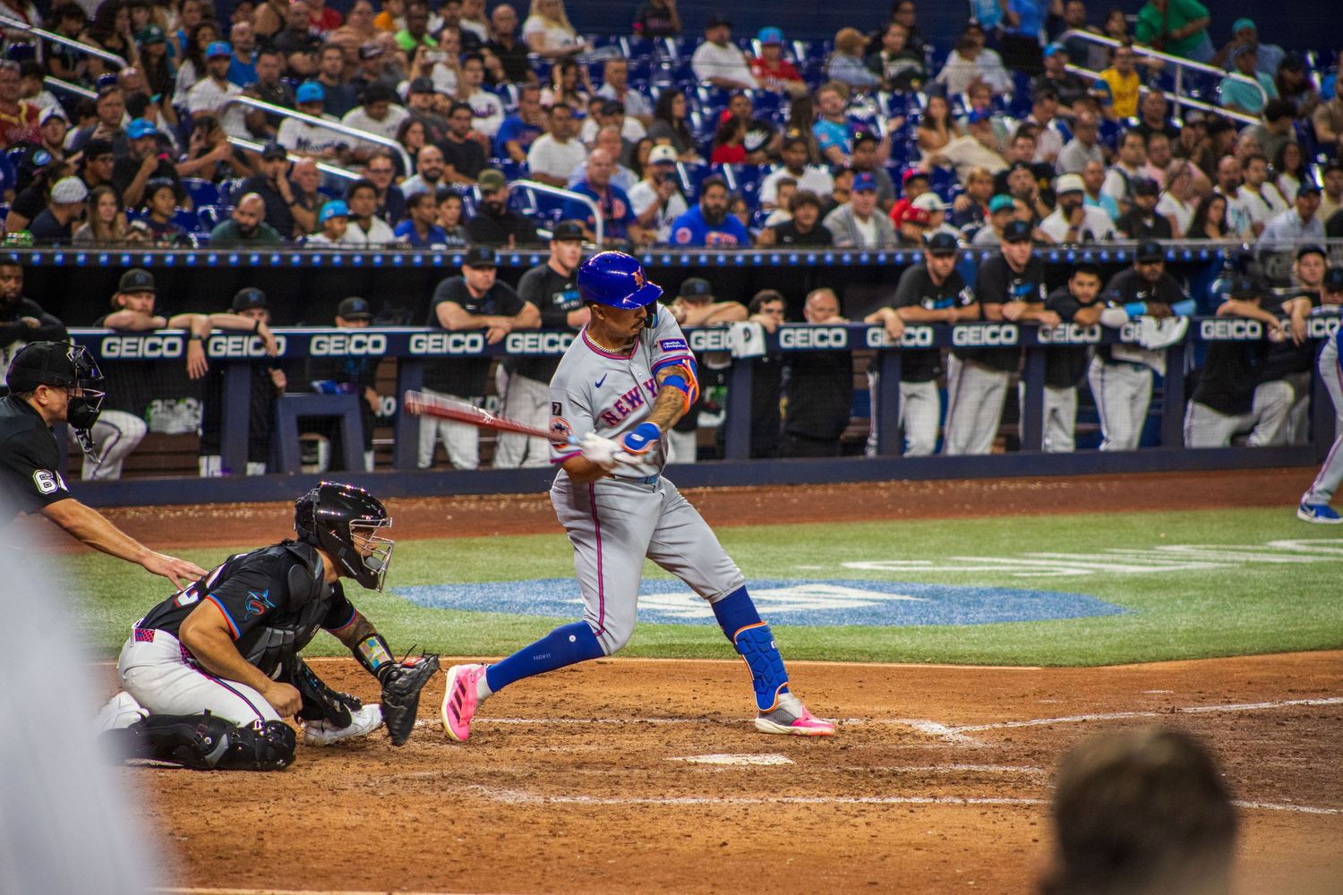 Baseball action at home plate during nighttime game with crowd watching in the background.