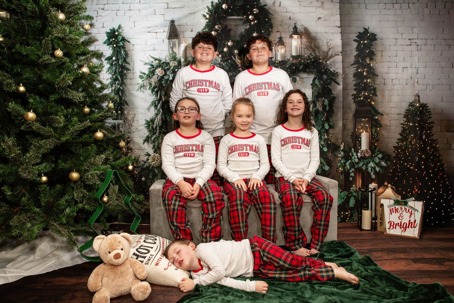 A family wearing matching plaid and white holiday outfits poses together for Christmas photos in front of a decorated tree.