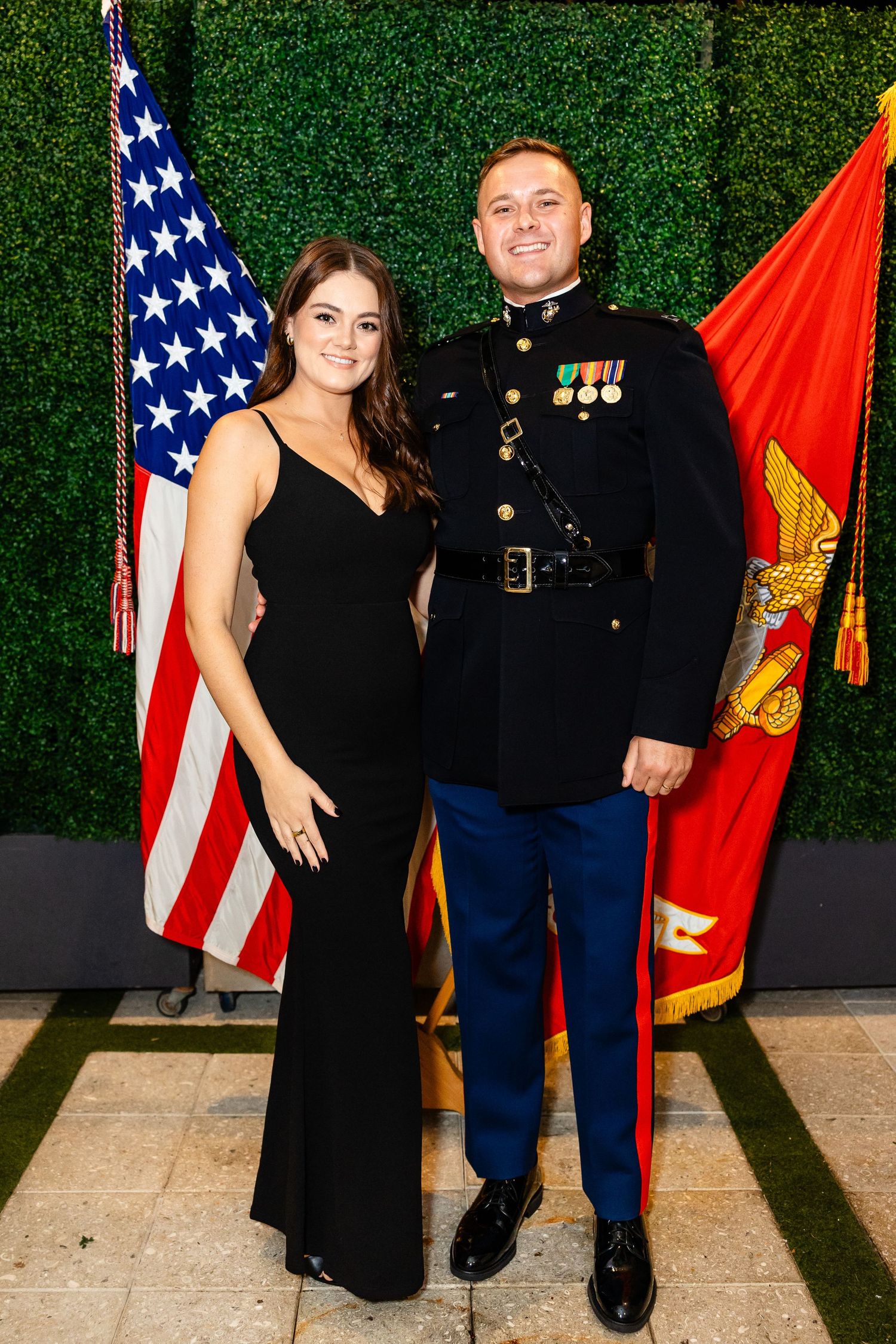 Marine Corps service members and guests pose for formal photos at a military ball with flags in the background.