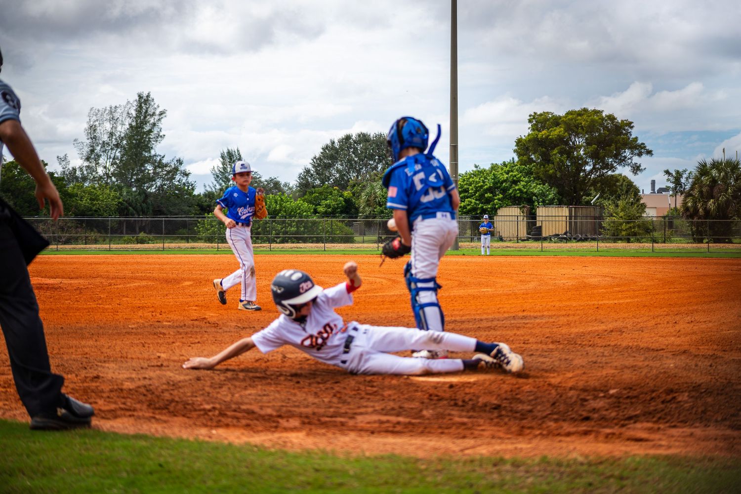Baseball player slides into base during intense game action on dirt infield.