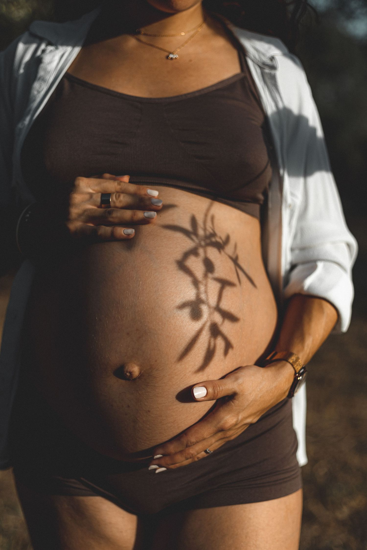 Femme enceinte au le ventre nu avec une chemise en coton blanche qui laisse apparaître un jeu d'ombre avec une branche d'olivier à Lourmarin