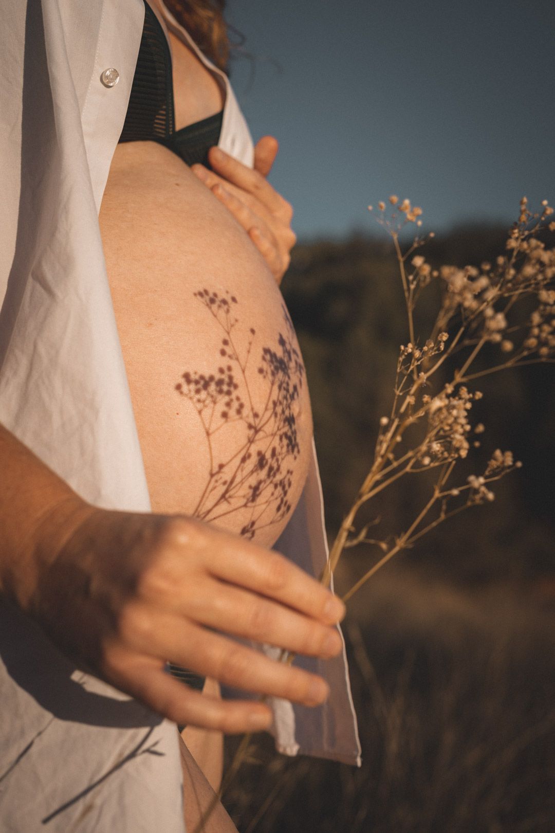 Femme enceinte au le ventre nu avec une chemise en coton blanche qui laisse apparaître un jeu d'ombre avec des fleurs à la Sainte-Victoire